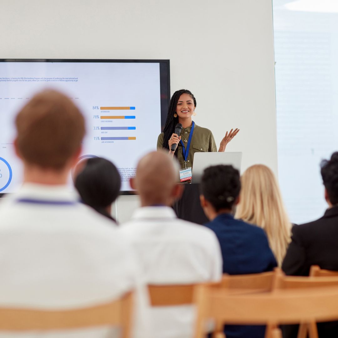 A woman in front of a room full of professionals setting recruitment goals.